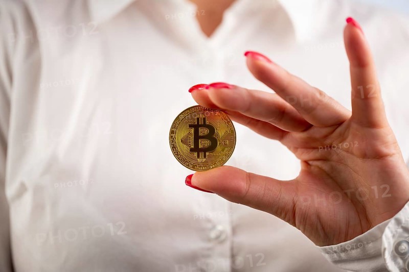Virtual cryptocurrency money Bitcoin golden coin in the left hand of a woman with red nail polish. The future of money