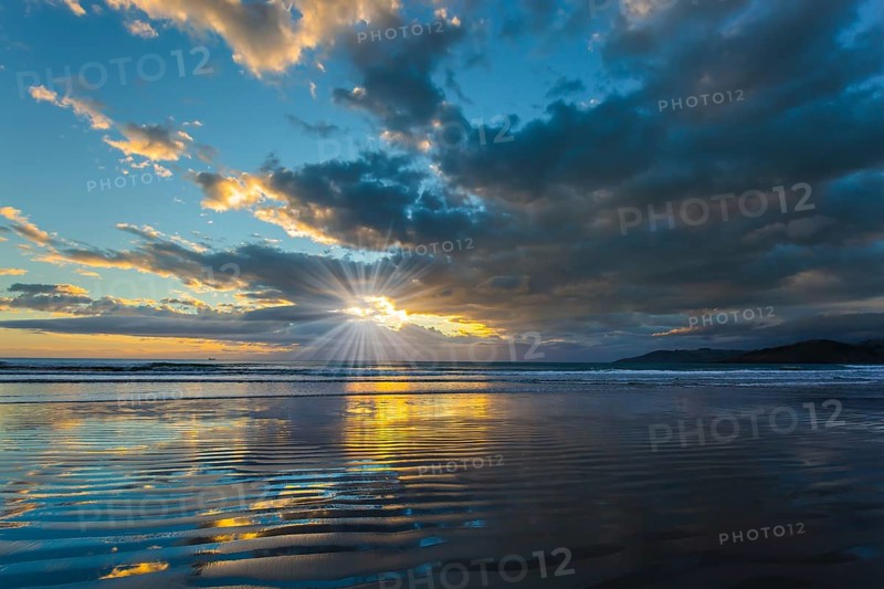 Sunrise over the ocean. Gentle cloud colors are reflected in the ocean water. Light wind causes small ripples in the water. The sun's rays make their way through the light morning clouds. Concept of artistic photography