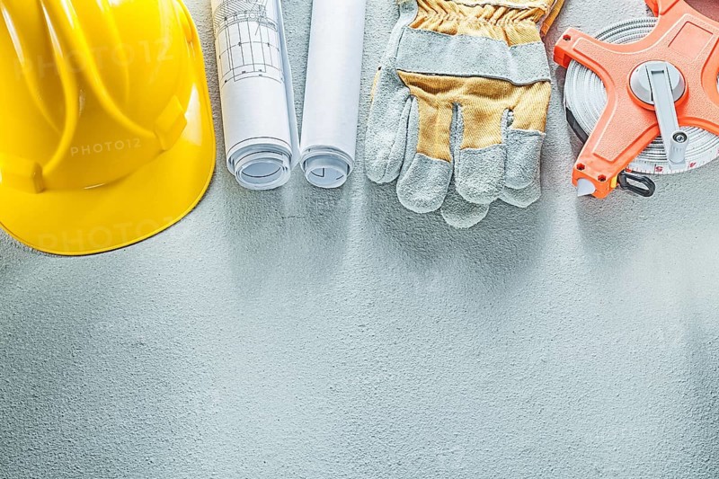 Safety gloves hard hats blueprints measuring tape on concrete background