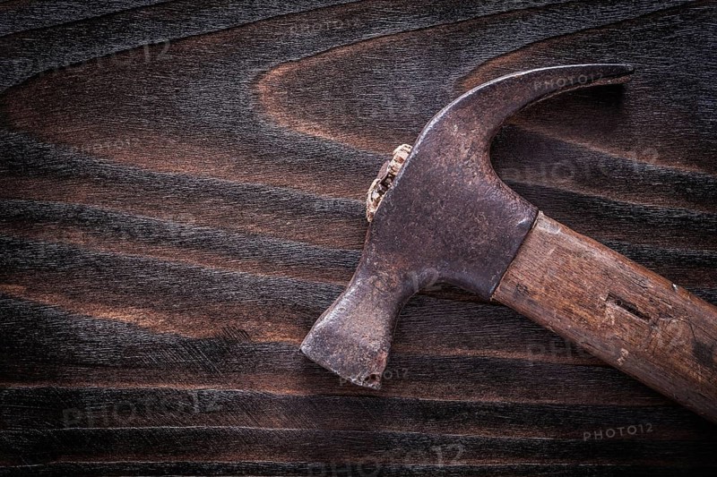 Rusty metal claw hammer with wooden handle on vintage dark wooden board construction concept