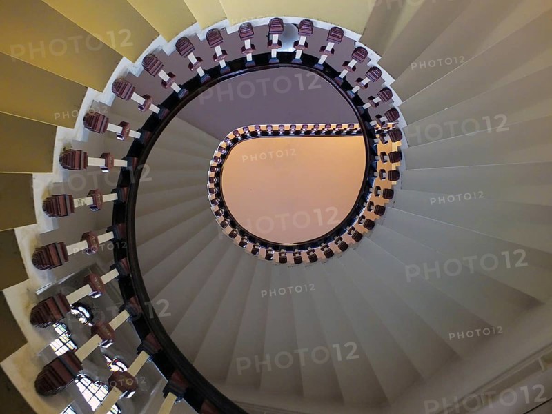 A looking upwards view of an elegant spiral staircase with wooden bannisters in elegant shades of white