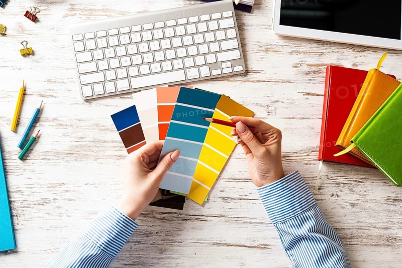 Interior designer choosing colors from swatches at wooden desk. Office workplace with computer keyboard. Selection of color palette for design. Professional house renovation and interior redesign