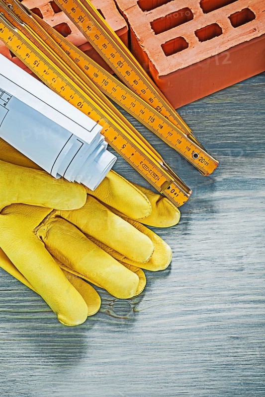 Composition of red bricks protective gloves blueprints wooden meter on wood board bricklaying concept