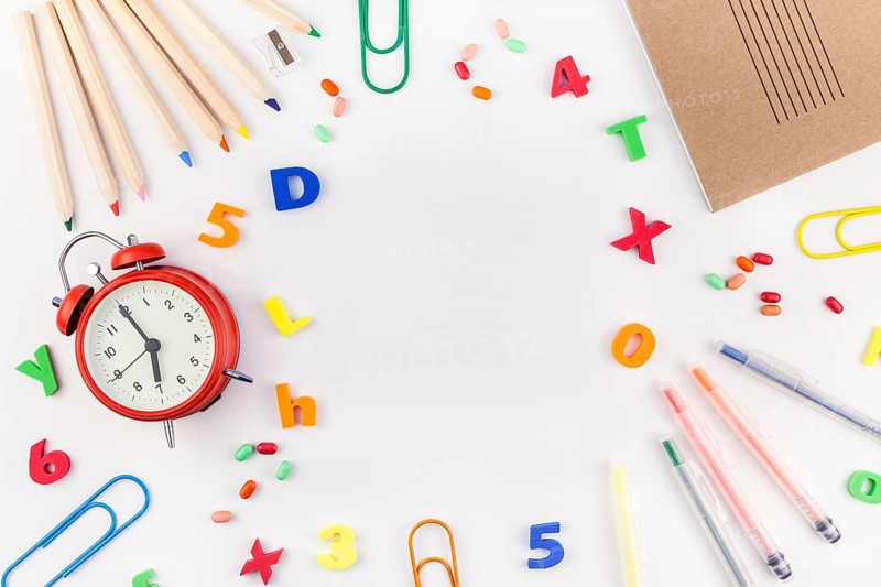 Creative flat lay back to school concept with alarm clock, color school and office supplies on white table background with copy space, frame, template for text or design
