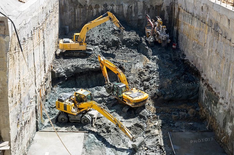 Excavators dig at a construction site of a street and a subway. Baggers transport dirt to a higher level to make room for the subway digging machine. Working fast and efficient
