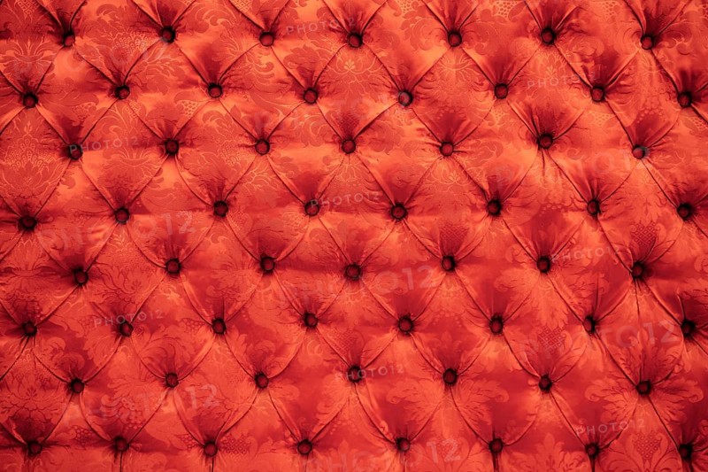 Close up background texture of scarlet red capitone genuine leather, retro Chesterfield style soft tufted furniture upholstery with deep diamond pattern and buttons.