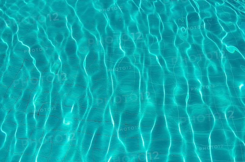Waves on the light of the pool water. Swimming pool with blue water. Water surface texture. View from above.