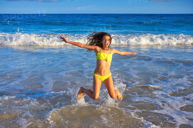 Bikini teen girl jumping happyt in Caribbean sunset beach splashing shore
