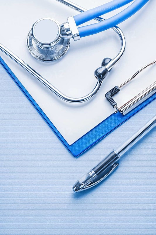 Ballpoint pen and stetoscope with clipboard on blue background medical concept