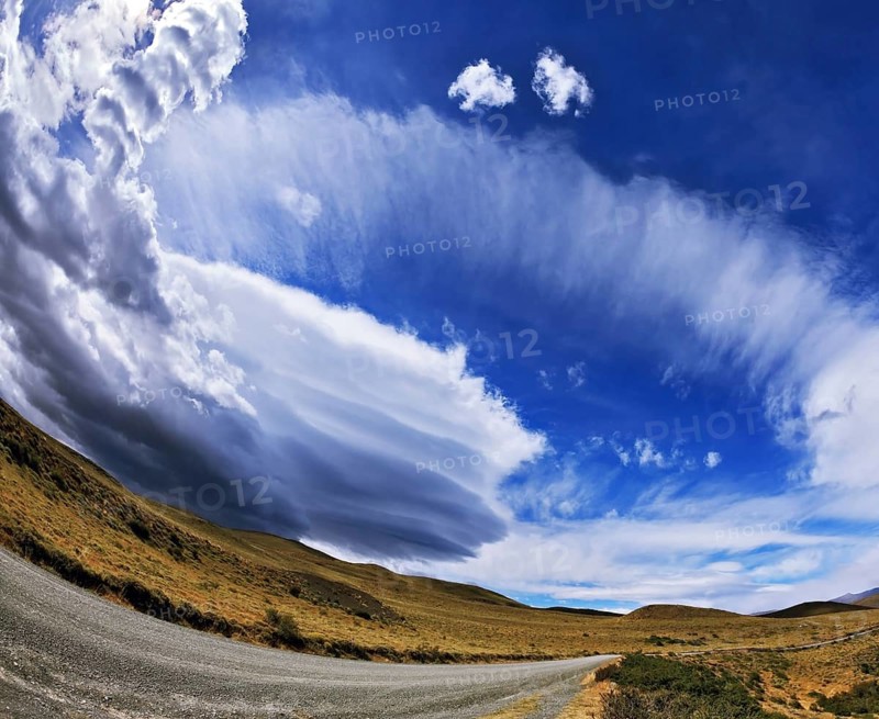 Gray dirt road in the Chilean national park to Torres del Paine. Improbable form the clouds created by glaciers, shine under the sun. On the horizon mountains with snow tops are visible. The photo is made a lens the Fish eye