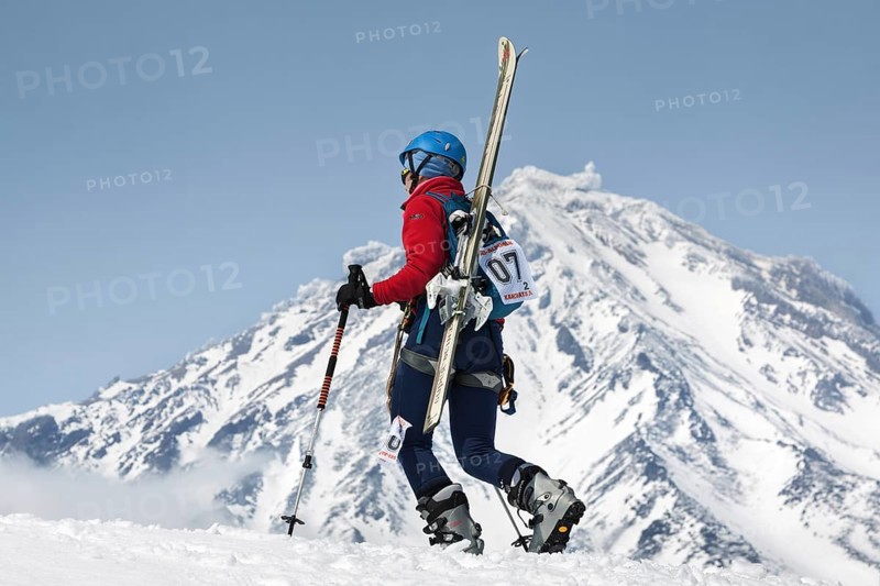 AVACHA VOLCANO, KAMCHATKA, RUSSIA, APR 21, 2012: Open Cup of Russia on ski-mountaineering. Girl ski mountaineer climbing on mountain with skis strapped to backpack on background active Koryak Volcano