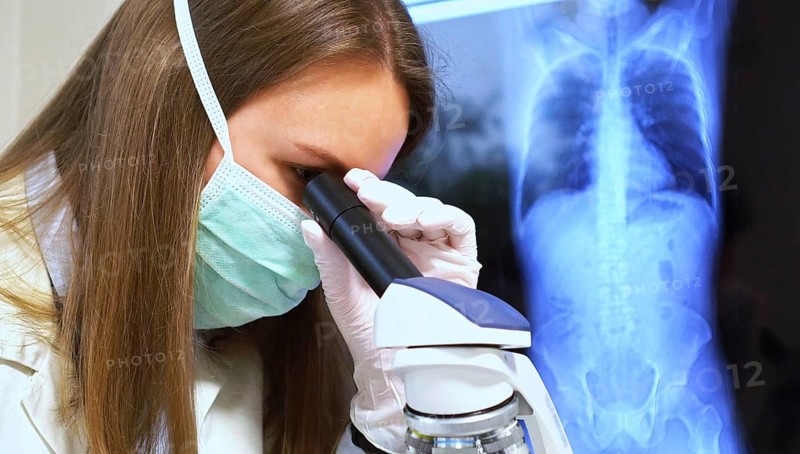 Scientist in medical mask in laboratory. Chest x-ray film on background