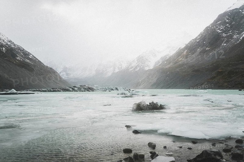 Mountain valley with frozen lake, surrounded by snow-capped mountains under a cloudy sky, Hooker Valley Track, New Zealand, Oceania