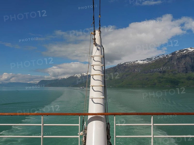 View from a boat access area over green water and surrounded by mountains and clouds, sailing in a fjord with green water and snow-capped mountains, Eidfjord, Norway, Europe