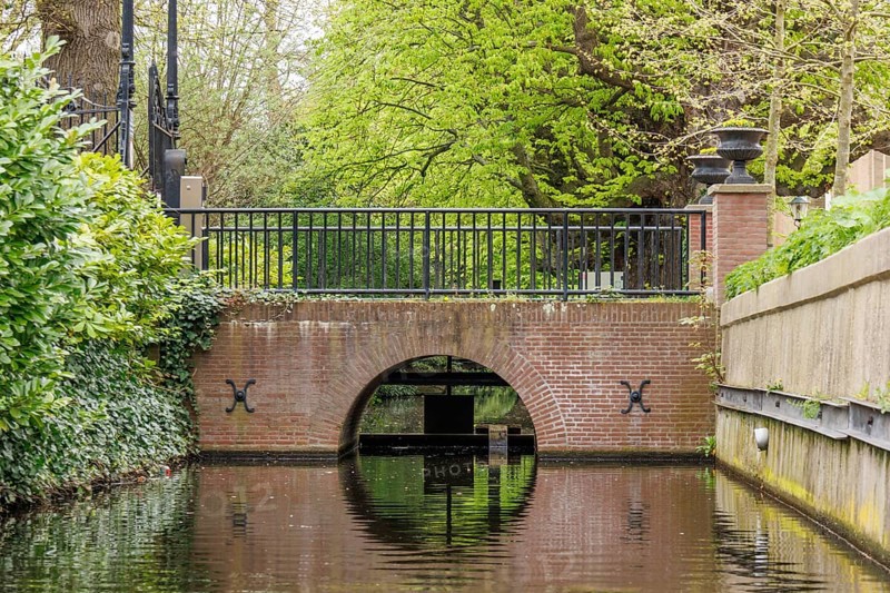 Small canal with a brick arch bridge and lush vegetation along the banks, den haag, the netherlands