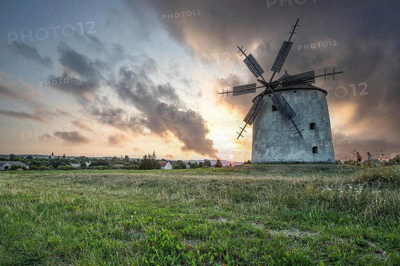 Windmill with wooden sails in a landscape with fields. Meadows and flowers appear in the sunset. Landscape shot in nature with a windmill. Historically atypical for the Balaton region in Hungary