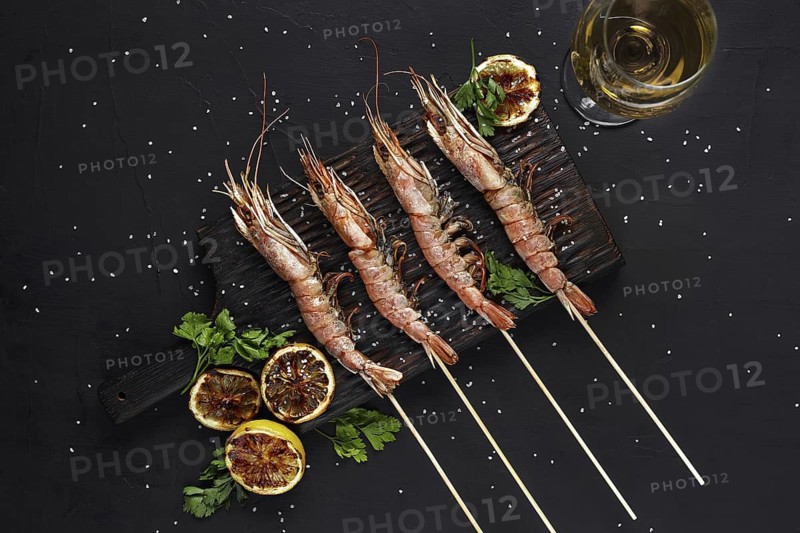Grilled shrimp skewers. Seafood, shellfish. Shrimps Prawns skewers with herbs, garlic and lemon on black stone background, copy space. Barbecue shrimps prawns