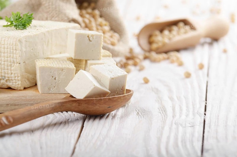 Soy Bean curd tofu on cutting board and in hemp sack on white wooden kitchen table. Space for text