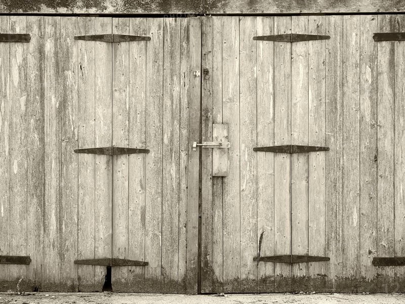 Monochrome old rural grey plank wooden plank doors with a bolt fastening and rusty iron hinges