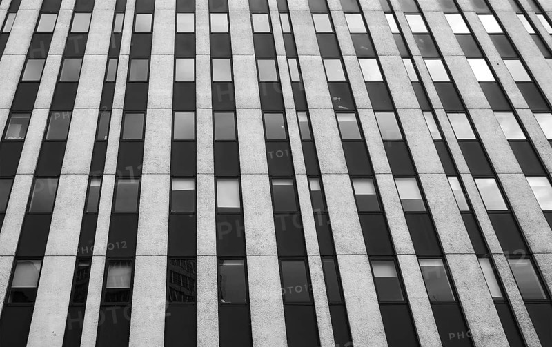 Close up perspective detail of tall high rise brutalist style office building with white vertical concrete lines and dark windows
