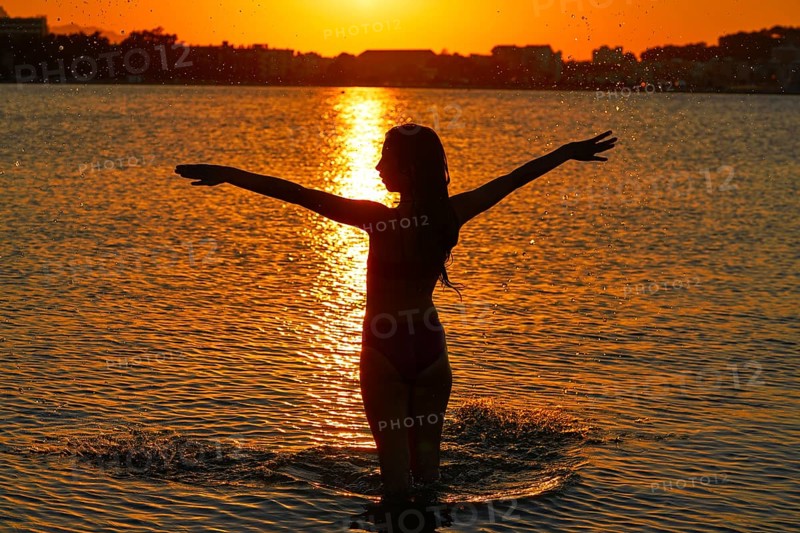 Girl silhouette at beach sunset open arms standing