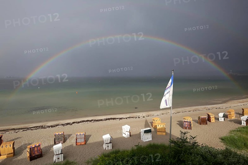 Rainbow over the sea, beach with beach chairs under a cloudy sky at the beach of Eckernförde