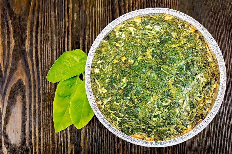 Celtic cake with spinach, tomatoes, oatmeal and eggs in baking dish from a foil, spinach leaves on the background of wooden boards on top