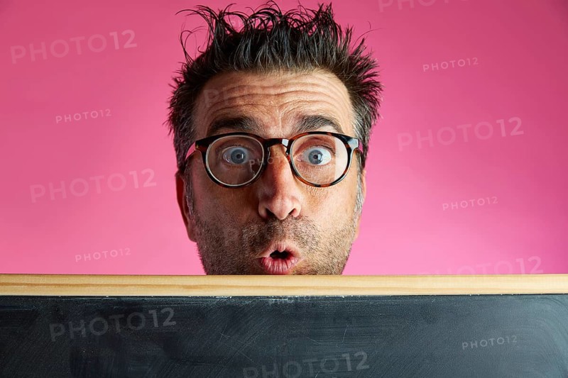 Nerd man crazy behind a blackboard funny surprise gesture in pink background