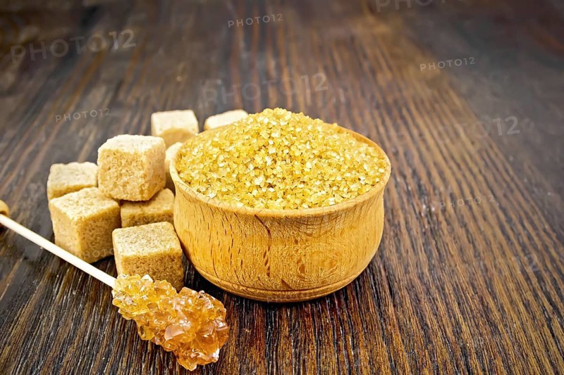 Granulated brown sugar in a bowl, crystalline on a stick and diced on a dark wooden board background