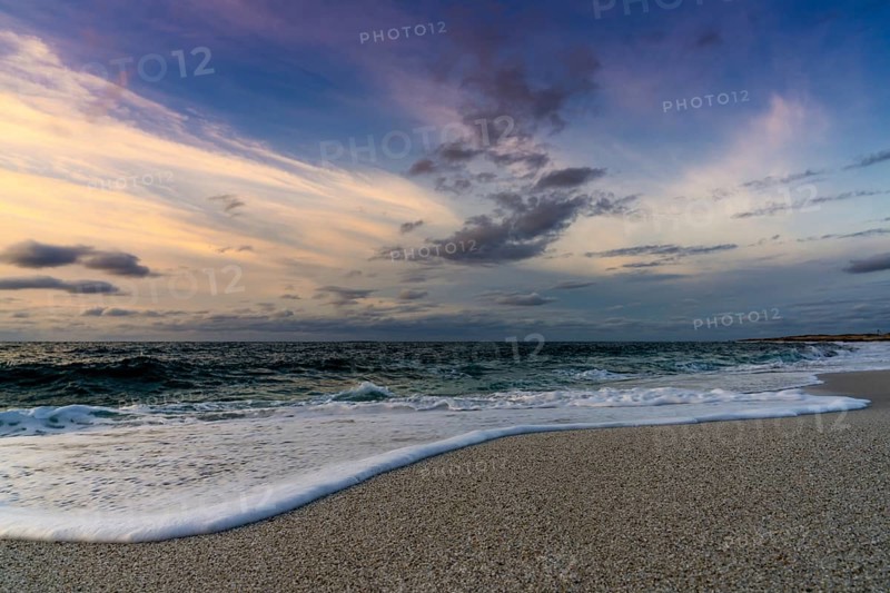 A low angle view of white sand beach with waves rolling in under a colorful sunset sky