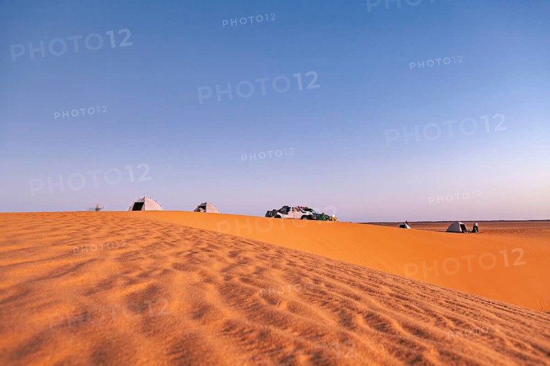 Tents and cars standing on a sand dune in the desert under a wide sky at sunset, camping in the sand dunes of the Sahara in Algeria