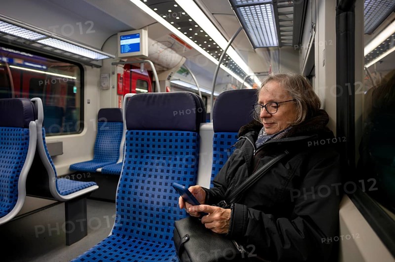 Elderly woman sitting in suburban train, train, operating mobile phone, smartphone, smiling, Stuttgart, Baden-Württemberg, Germany