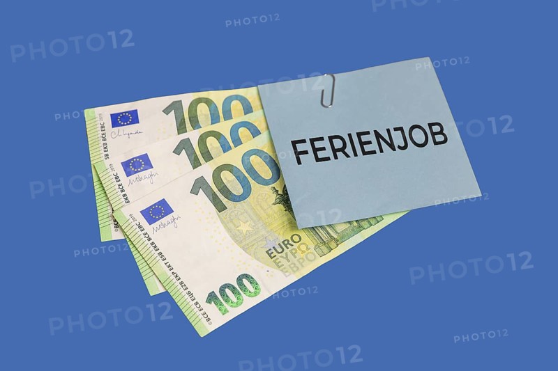 Holiday job symbol image: euro banknotes and a piece of paper with the words HOLIDAY JOB cut out against a blue background