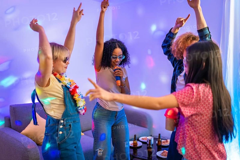Group of diverse friends enjoying karaoke night, singing and dancing together in a colorful, illuminated living room
