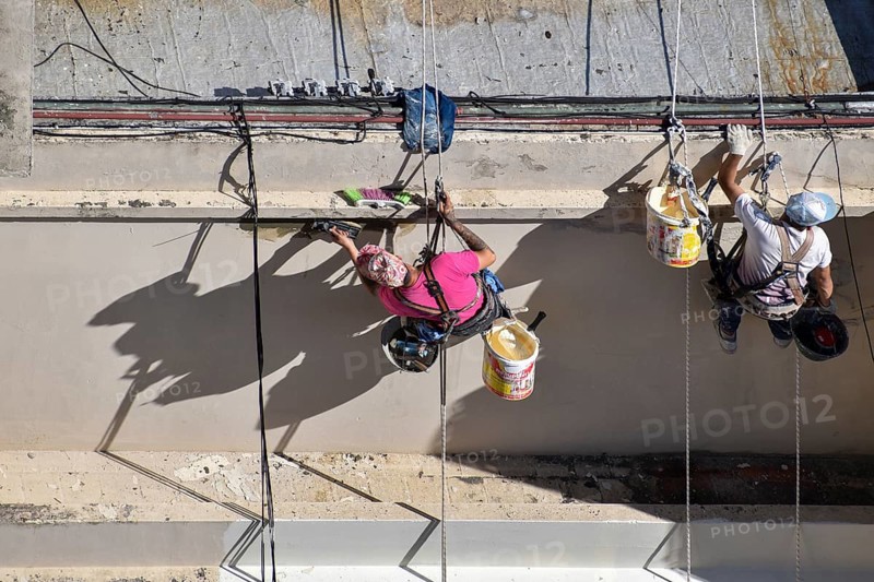 Painter hanging from a rope while working on a façade, symbolic image for safety in construction, Buenos Aires, Argentina