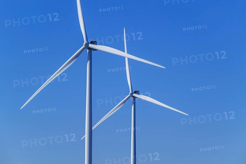 Two wind turbines showing tower, nacelle and huge rotor blades against blue sky