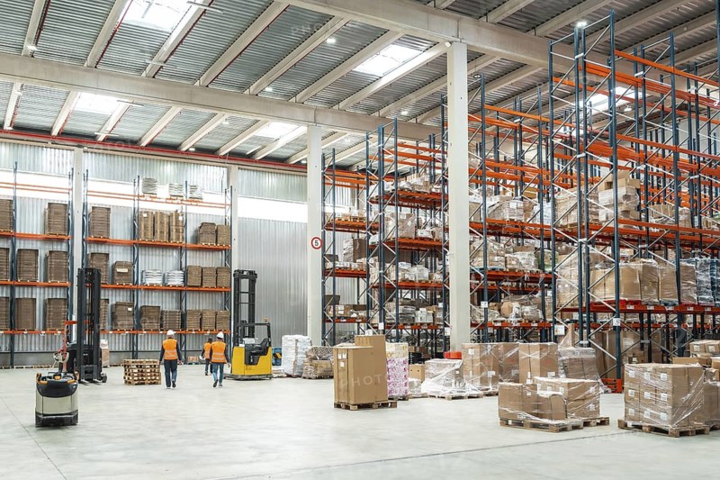 Warehouse workers are managing logistics, operating forklifts, and organizing packages on shelves in a distribution center