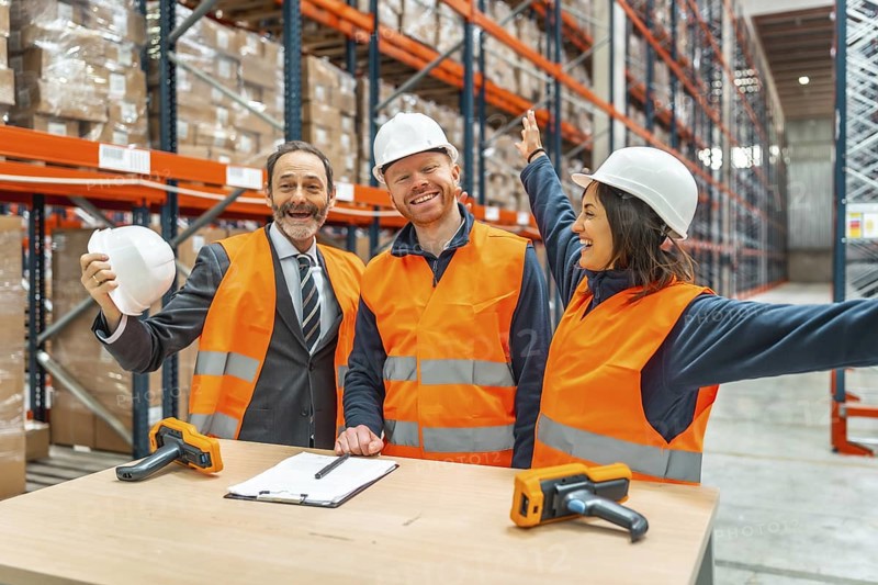 Warehouse workers and their manager are celebrating a successful logistics operation, expressing joy and teamwork in a modern storage facility