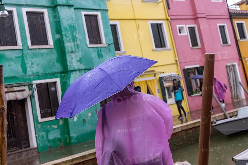City view of Burano with colourfully painted houses and canals. Rainy weather, people are carrying umbrellas. Burano, Venice, Venezia, Italy