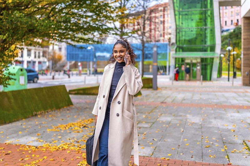 Happy african businesswoman talking to the mobile while walking along the city after work