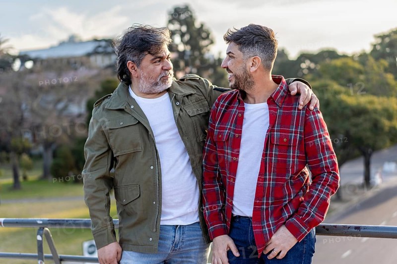 A smiling married couple, both men, embracing while having a conversation outdoors