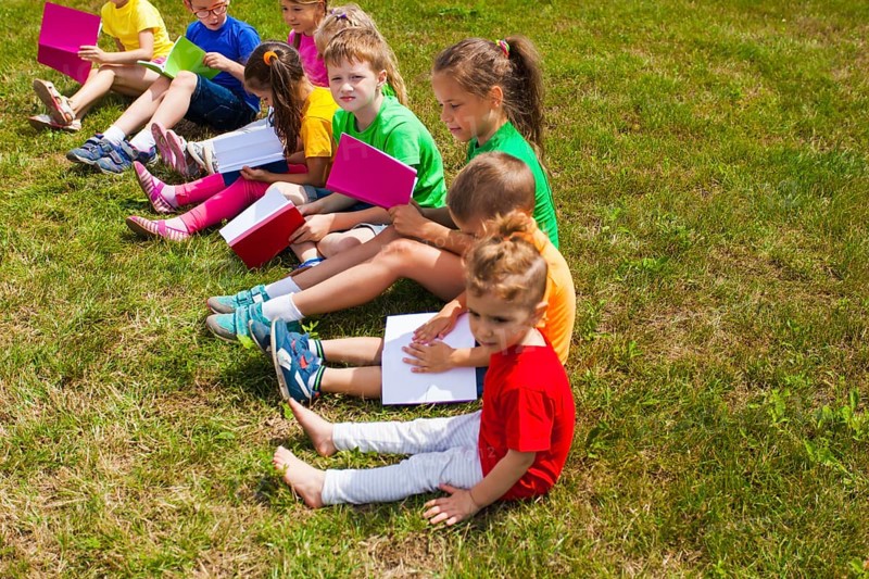 The good kids in colorful t-shirts sit on the grass with books in their hands