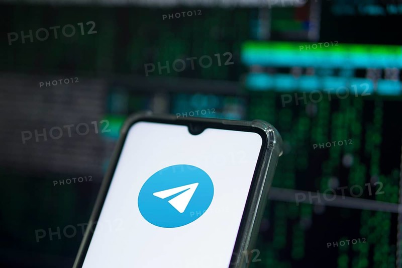 The TELEGRAM app logo on the screen of a cell phone that a man is holding.