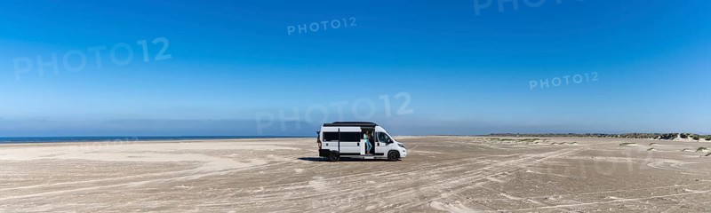 Ringby, Denmark: 31 May, 2021: panorama of a gray camper van parked on an endless white sand beach in the middle of nowhere with ocean behind