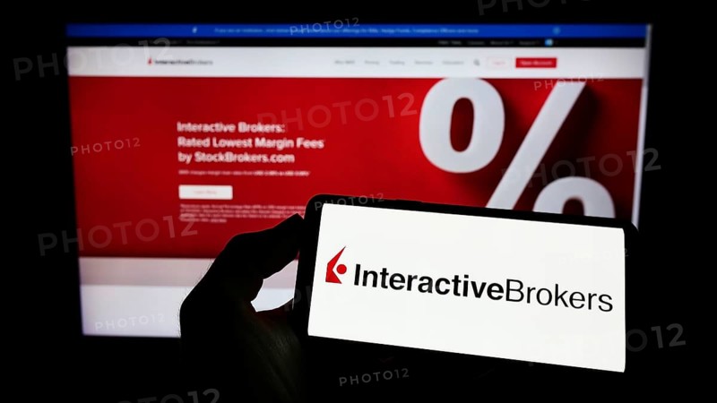 Stuttgart, Germany, 07-24-2022: Person holding mobile phone with logo of American company Interactive Brokers LLC (IB) on screen in front of web page. Focus on phone display