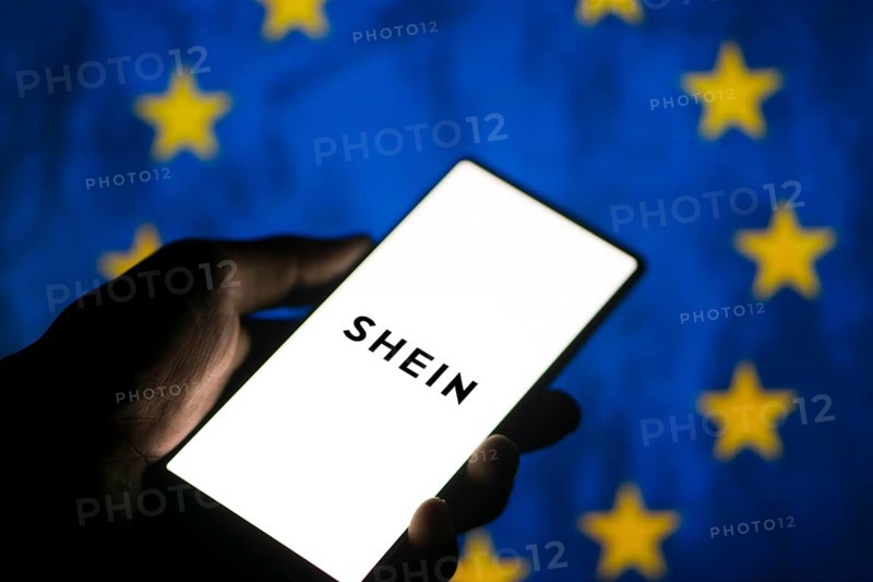 Smartphone with website of fashion e-commerce company Shein in front of business logo. Focus on top-left of phone display