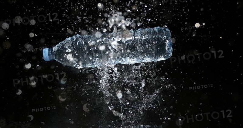 Bottle of Water falling on Water against Black Background