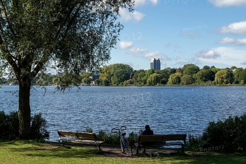 Leisure activities in summer, bicycle and woman on park bench, blue sky, Alster with Hotel Radisson, Hamburg, Germany