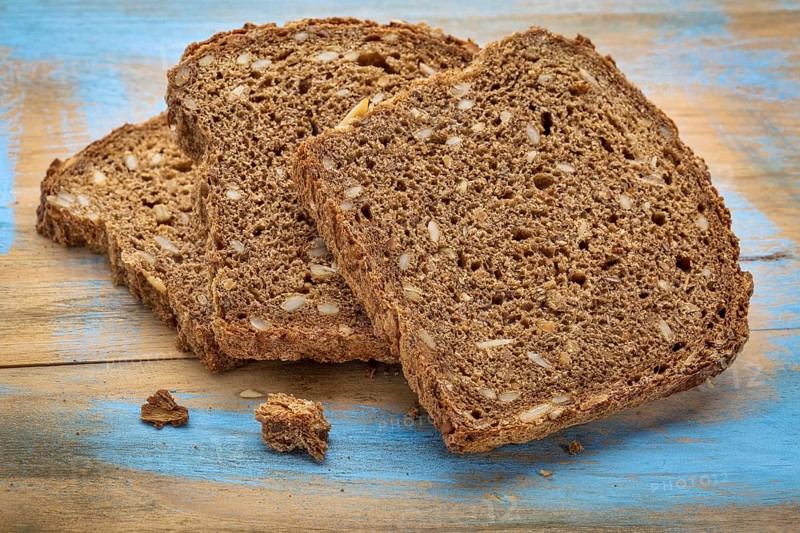 Slices of organic, whole grain, dark rye bread on painted wooden cutting board