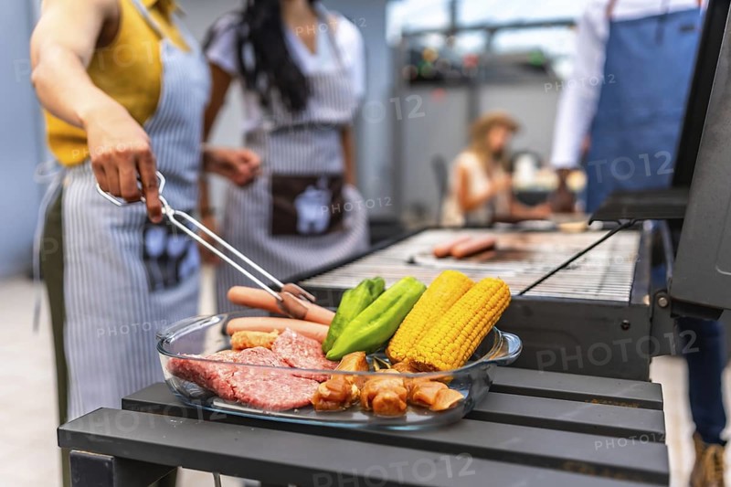Chefs preparing a barbecue with meat, corn and vegetables on a glass tray, ready to be grilled